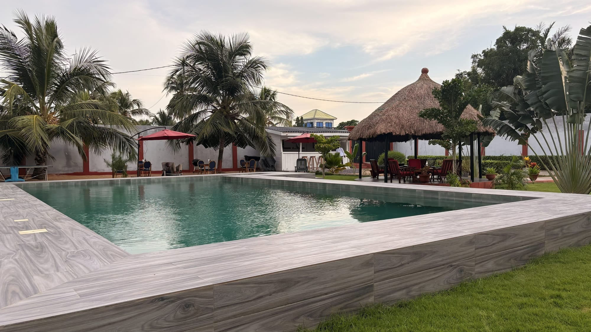 La piscine de Maison Stella entourée de palmiers et de la paillote, au couchant, à Avepozo (Lomé, Togo)